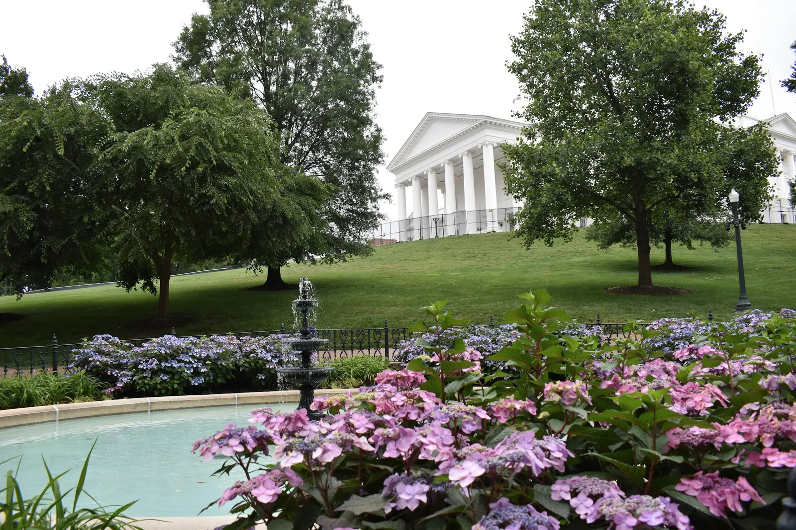 A fountain and spring flowers in a park in Richmond, with a white columned building behind the trees.